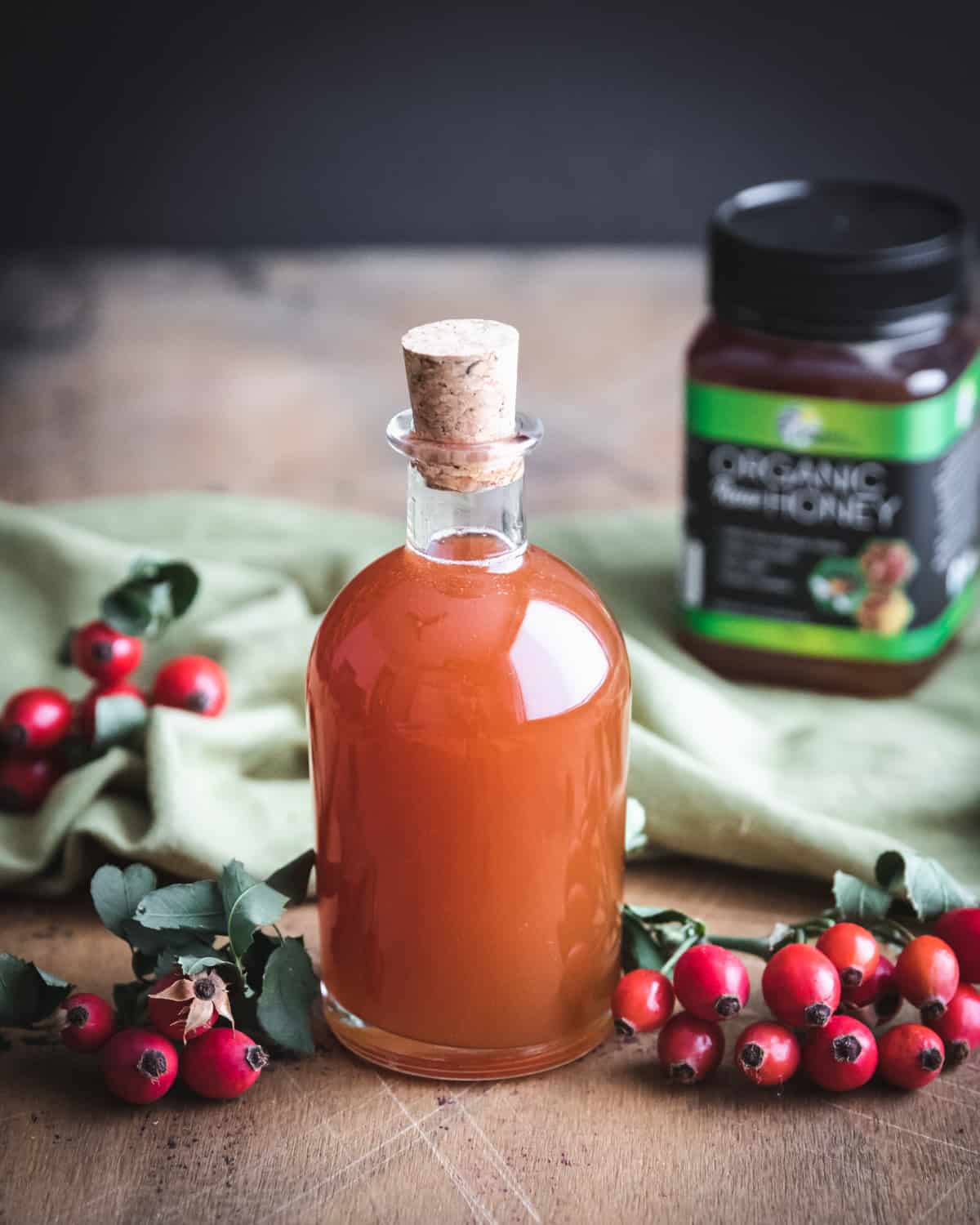 a bottle of rose hip syrup with a container of organic raw honey