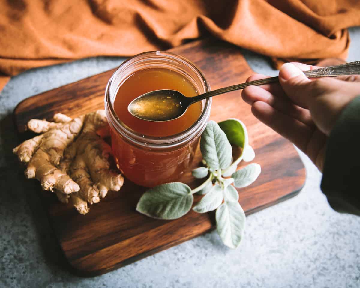 a hand holding a spoonful of sage and ginger oxymel