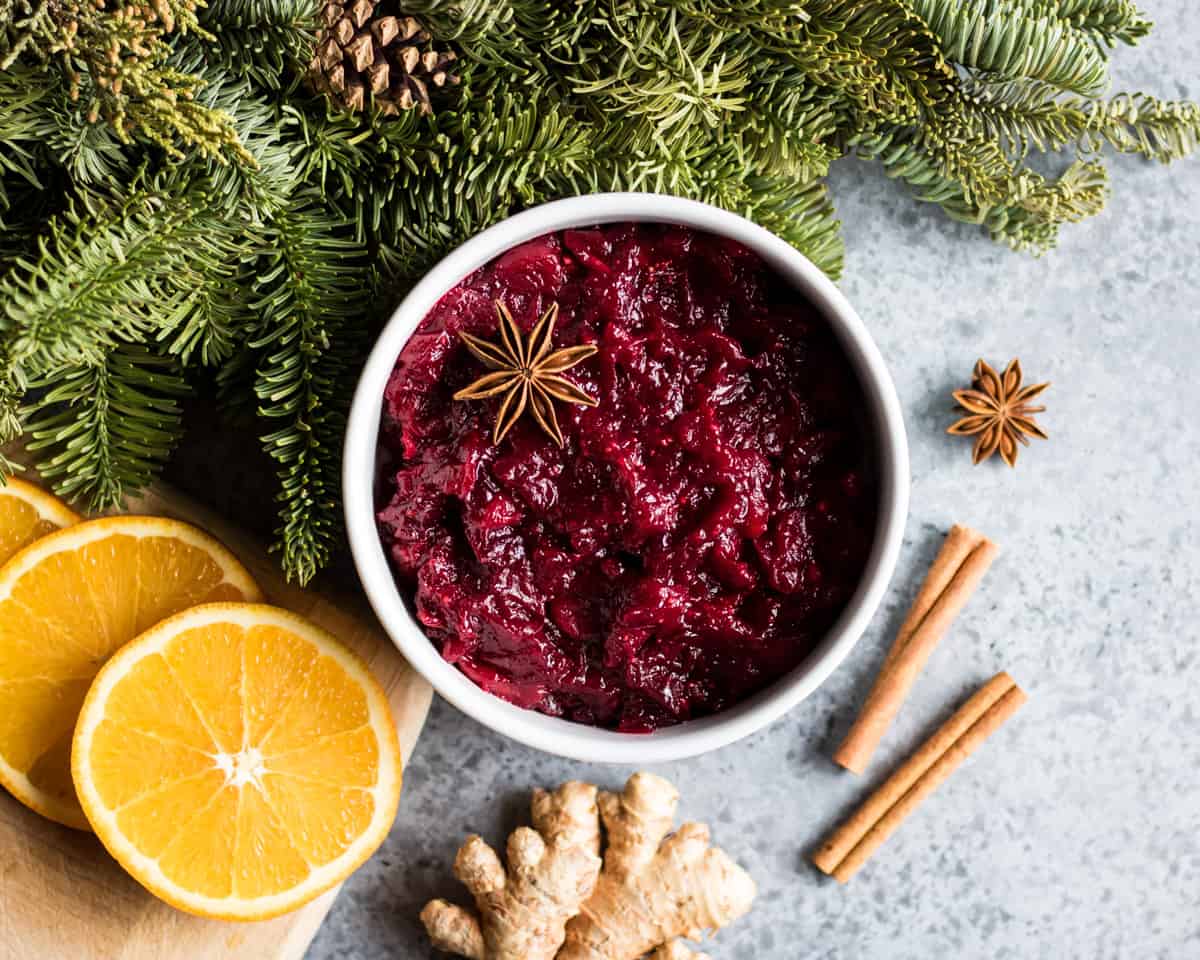 a bowl of spiced cranberry sauce on a table with a conifer branch