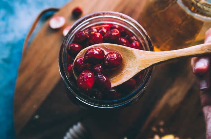 A jar of honey fermented cranberries with a wooden spoon lifting some out, top view. On a dark wood surface.