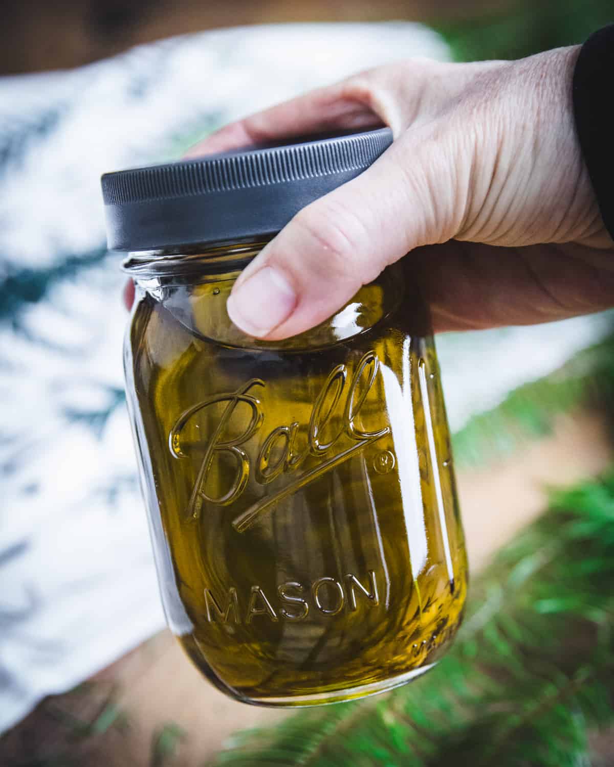 a hand holding a ball jar of infused conifer oil