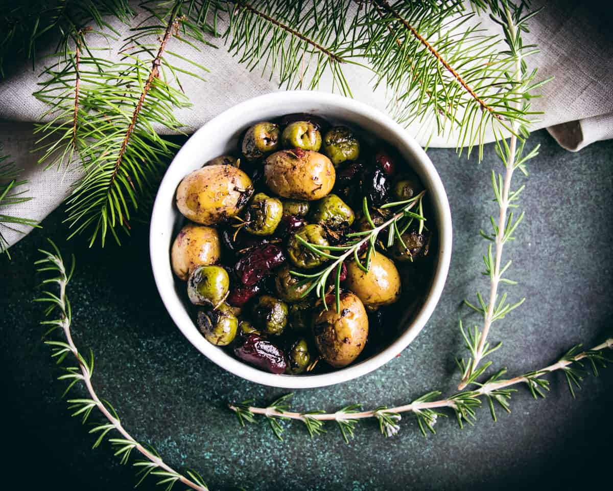 a bowl of roasted olives with rosemary garnish