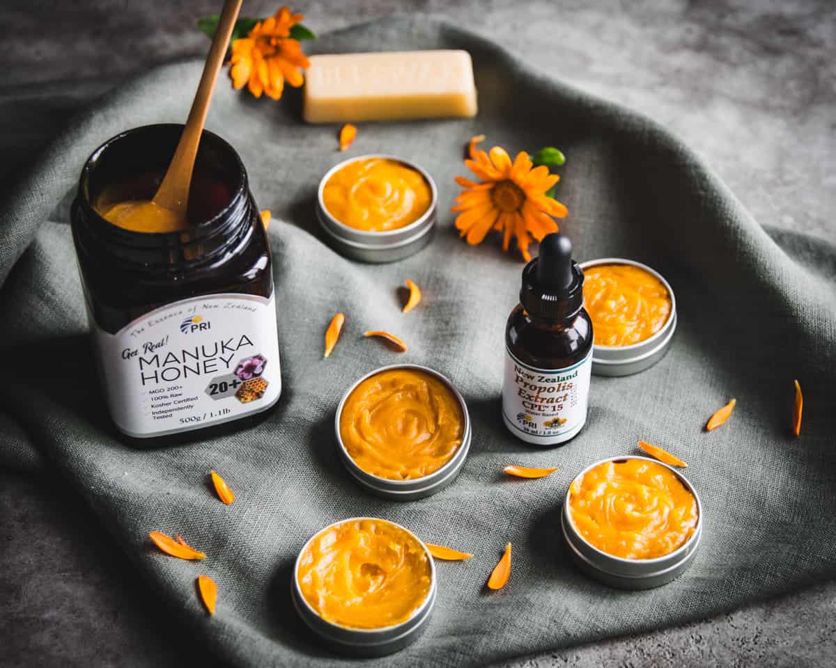 a jar of manuka honey and proplis with salves on a green cloth