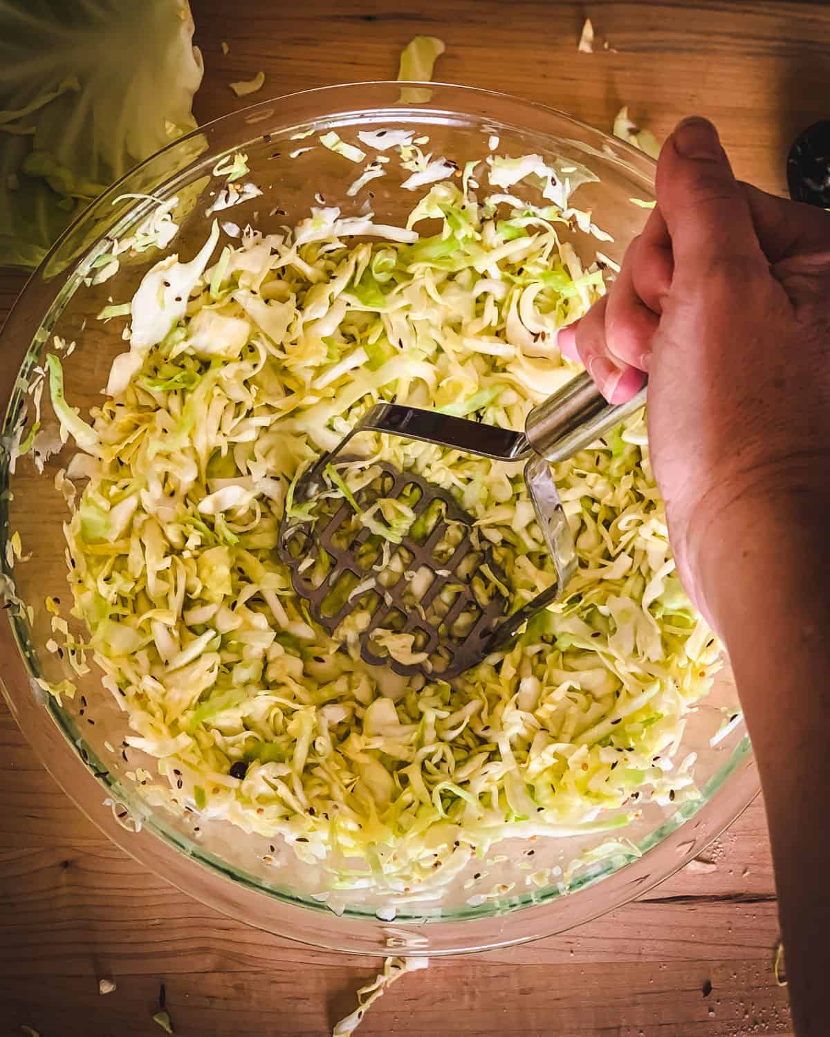 a hand mashing the cabbage with a potato masher