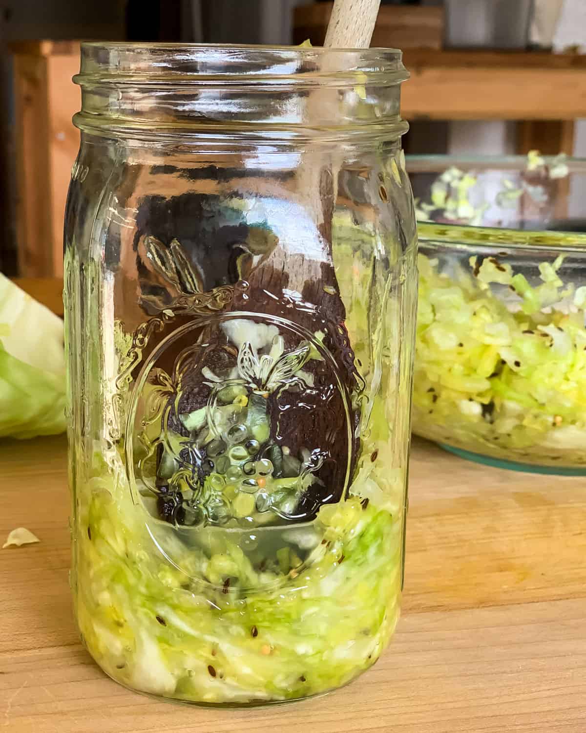 a wooden spoon packing the cabbage into a quart jar