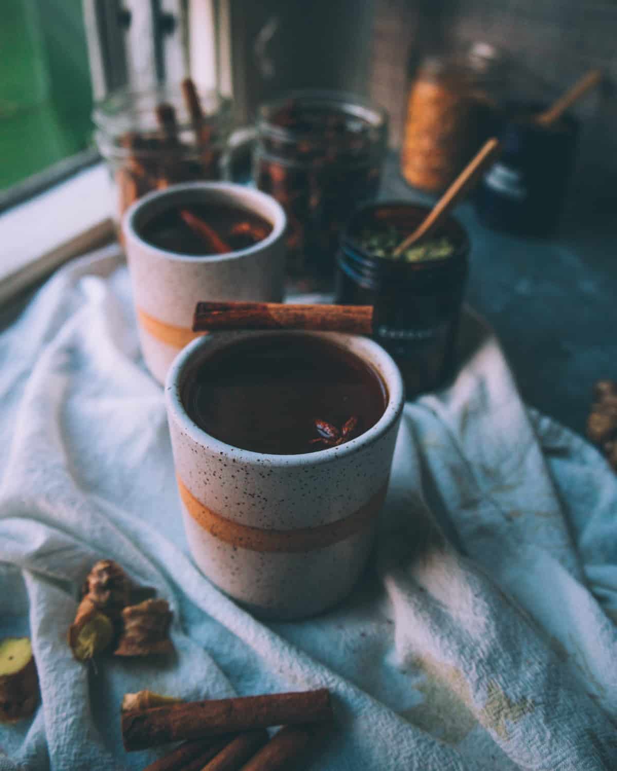 two mugs of black chai garnished with a cinnamon stick