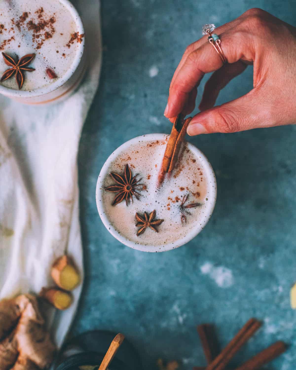 a woman's hand holding a cinnamon stick in a mug of hot chai with milk