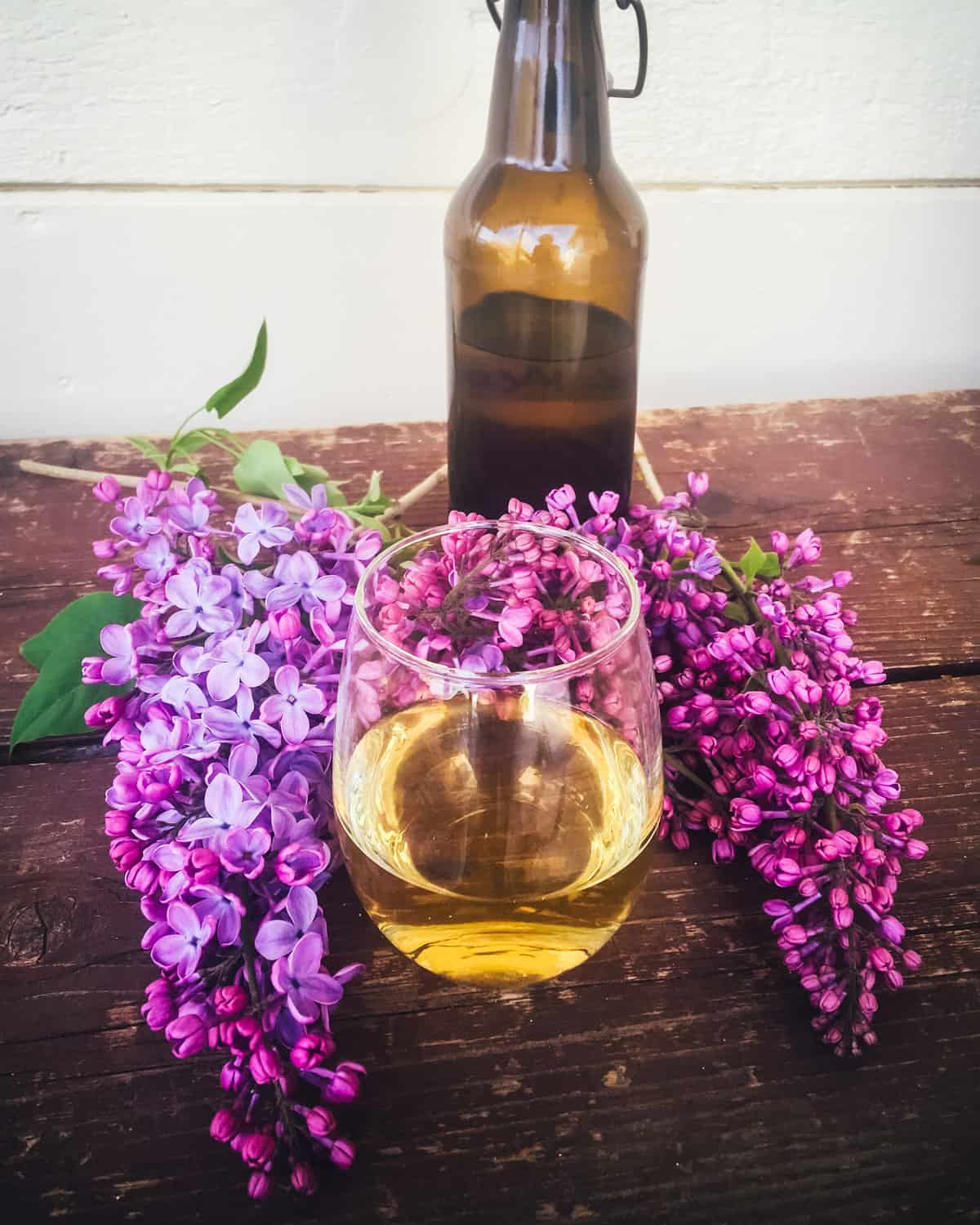 a bottle and glass of lilac mead on a table with lilac flowers