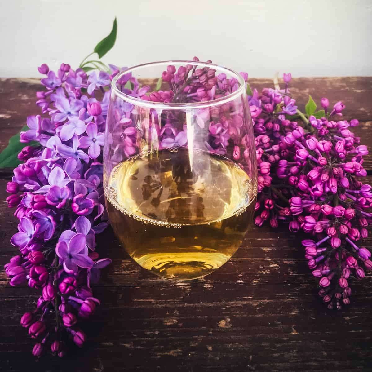 a glass of lilac mead on a table with lilac flowers