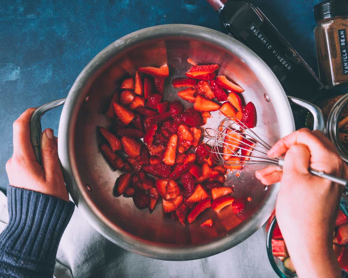 a woman's hand mashing up strawberries in a pot with a whick