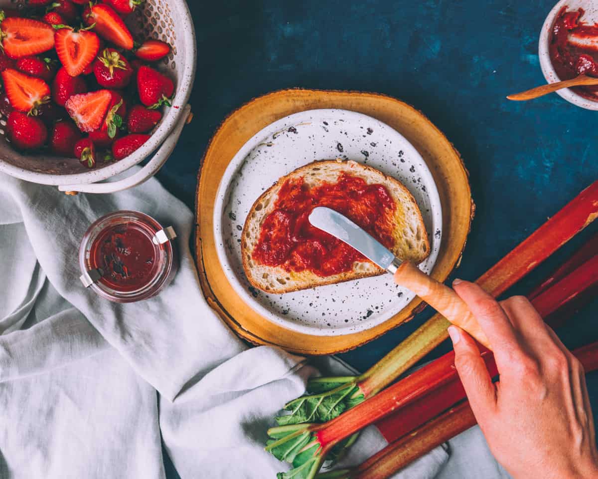 a knife spreading strawberrry rhubarb butter on toast