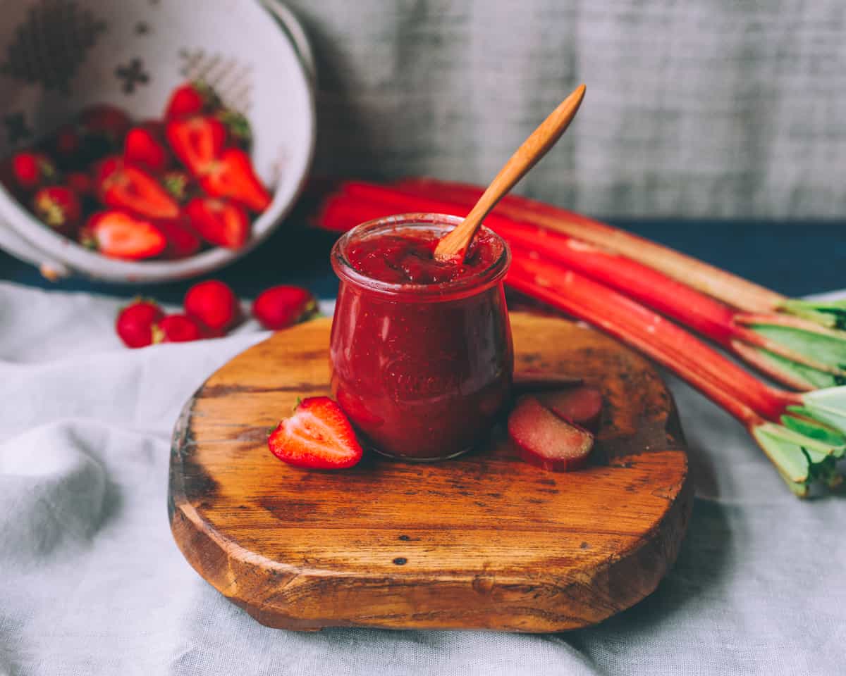 a jar of strawberry rhubarb butter on a wooden board