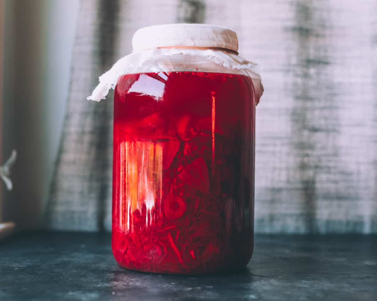 a gallon jar of fermenting strawberry rhubarb soda covered with cheesecloth