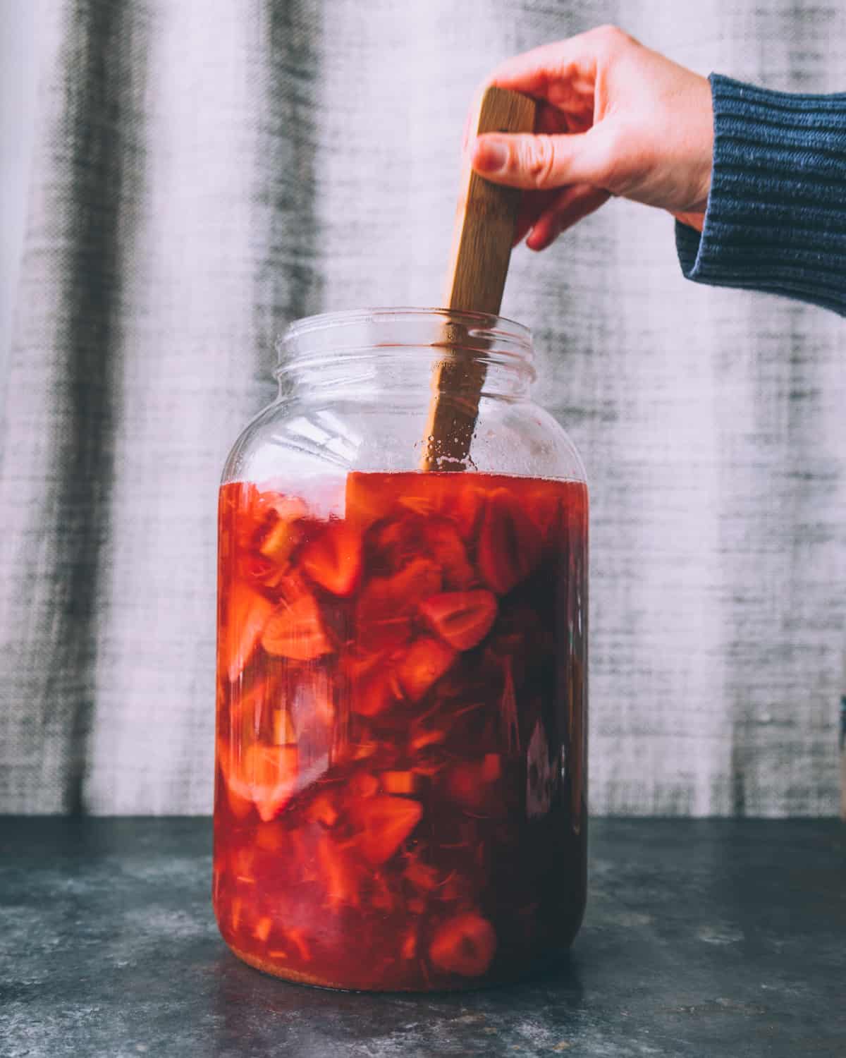 a woman's hand stirring the fermenting soda with a wooden spoon