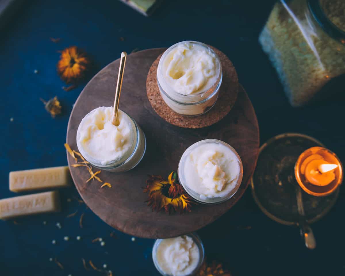 three glass jars of calendula cream on a round wooden table