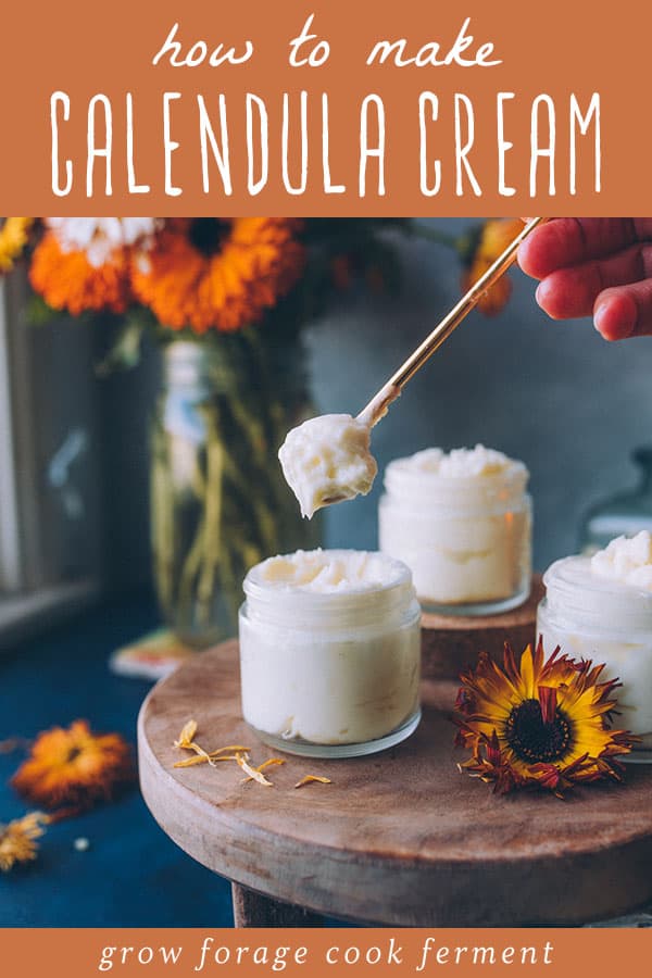 a womans hand scooping a spoonful of calendula cream from a glass jar