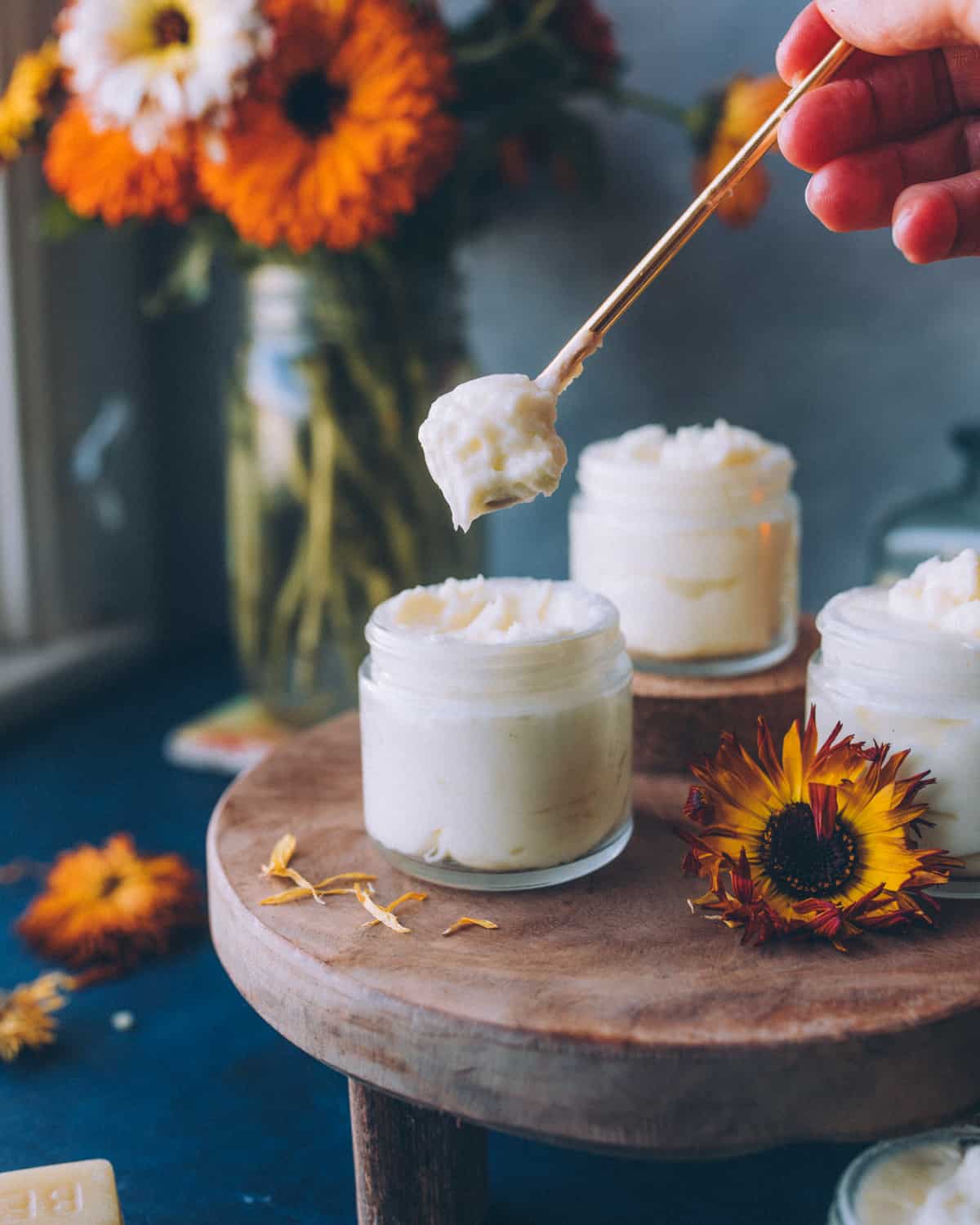 a hand holding a spoon of calendula cream above a jar