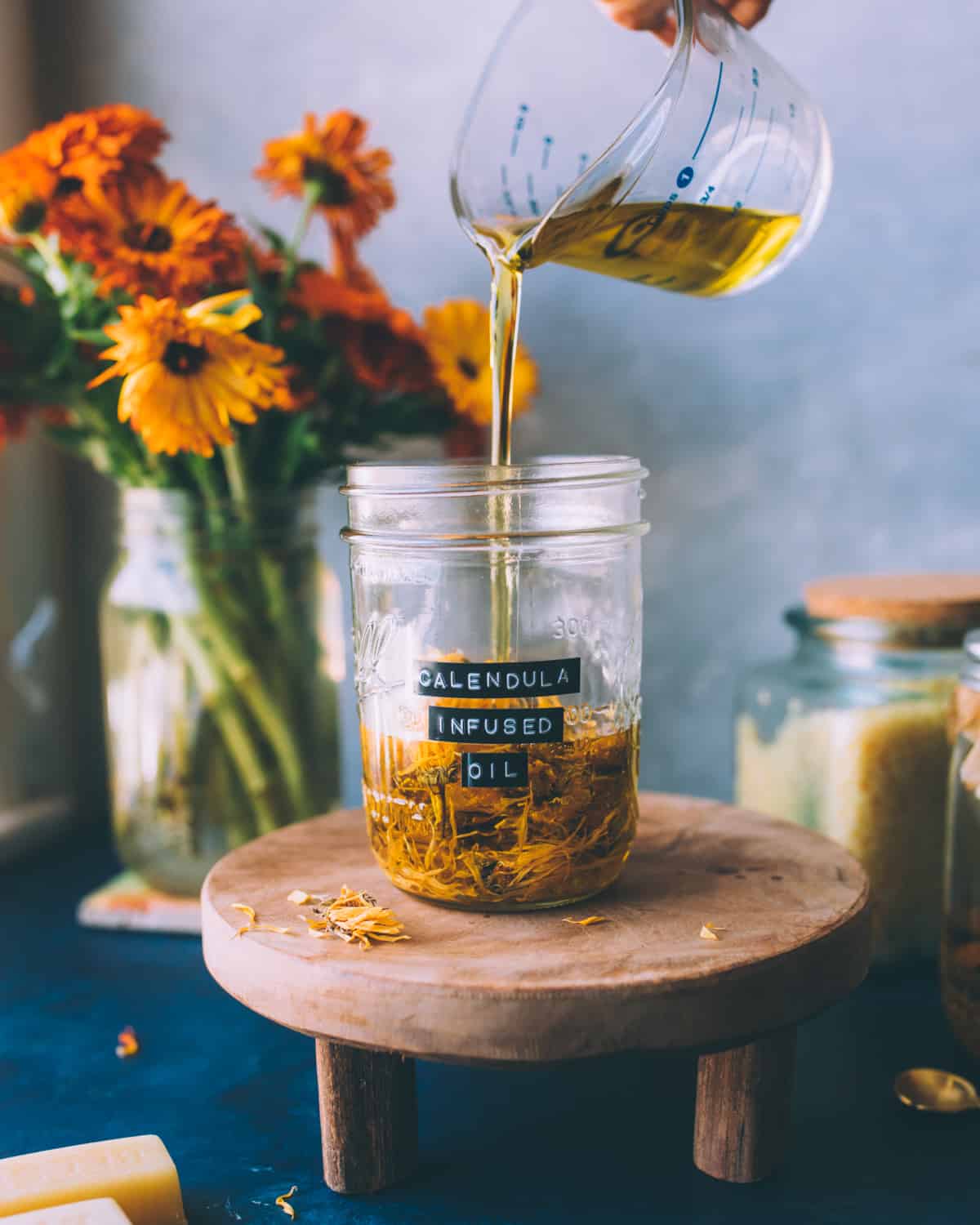 A small jar of calendula flowers with carrier oil being poured on top to infuse. 