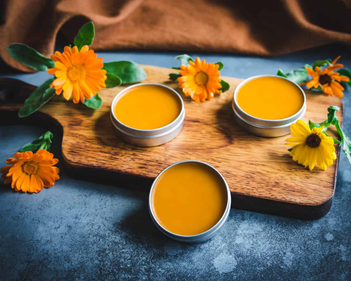 tins of calendula infused oil on a wooden cutting board