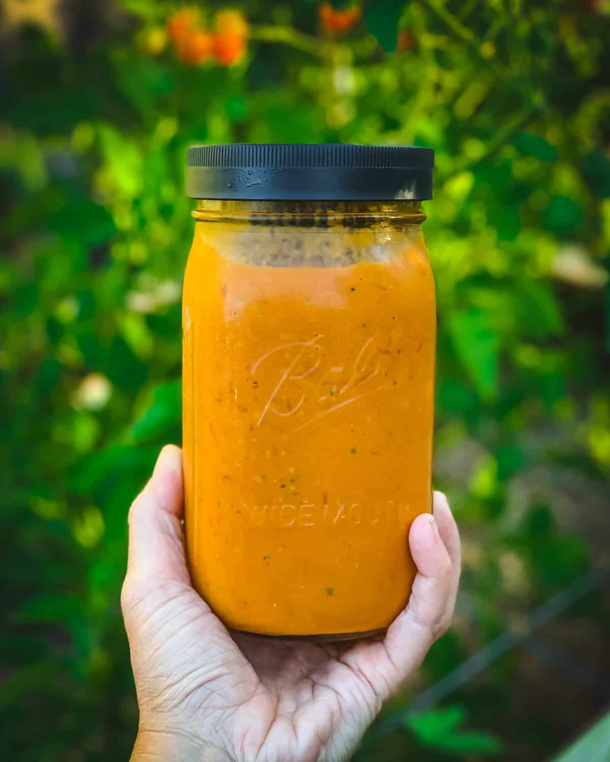 a hand holding a quart jar of roasted cherry tomato sauce