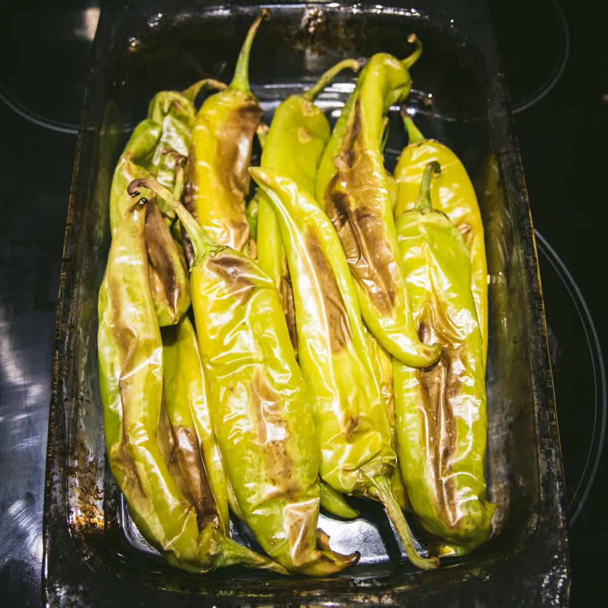 A pile of roasted hatch peppers with charred brown skin in a baking pan.