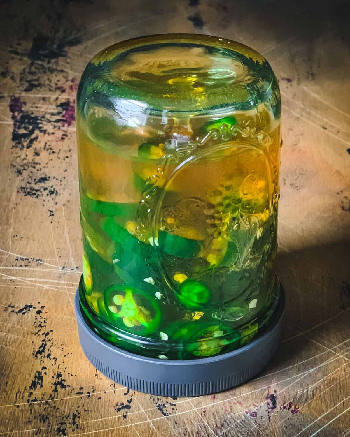 Jar filled with sliced jalapeños and honey, turned upside down resting on a wooden cutting board.