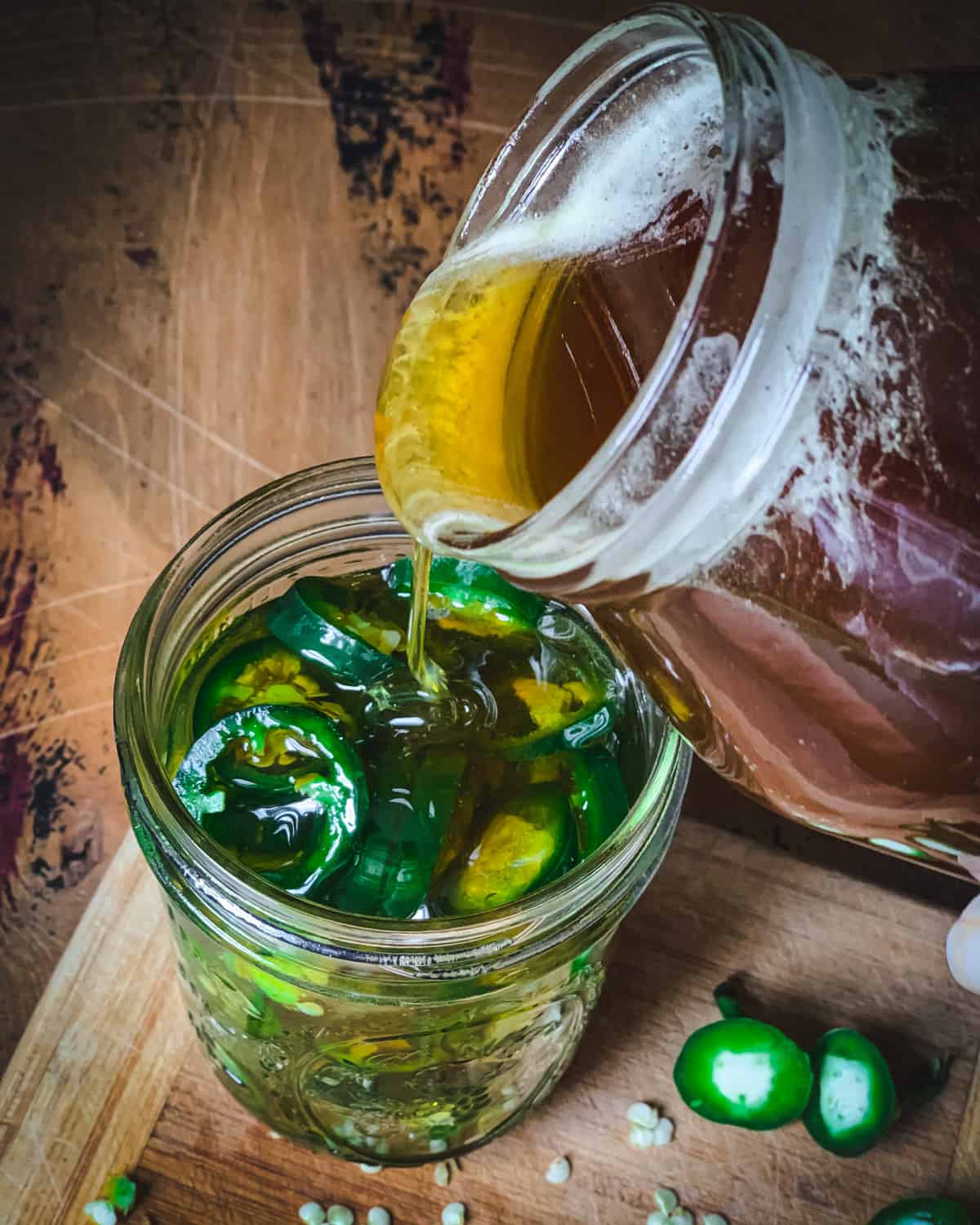 Big jar of honey pouring into smaller jar of sliced jalapeños.