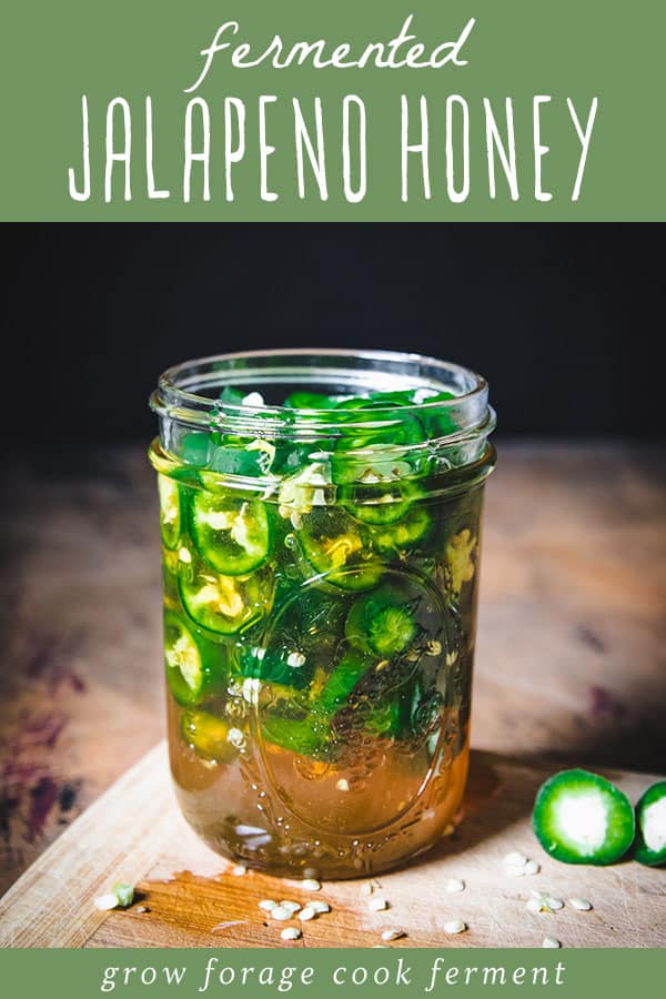 Top banner green with white words saying "fermented jalapeno honey" picture below shows jar with sliced green jalapeno peppers covered to the top with honey sitting atop a wood cutting board.