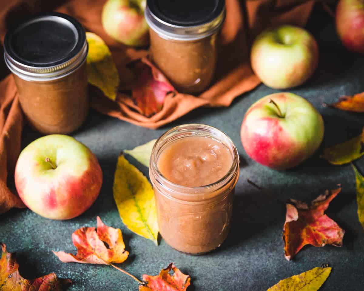 an opened jar of spiced maple apple butter with apples and leaves all around