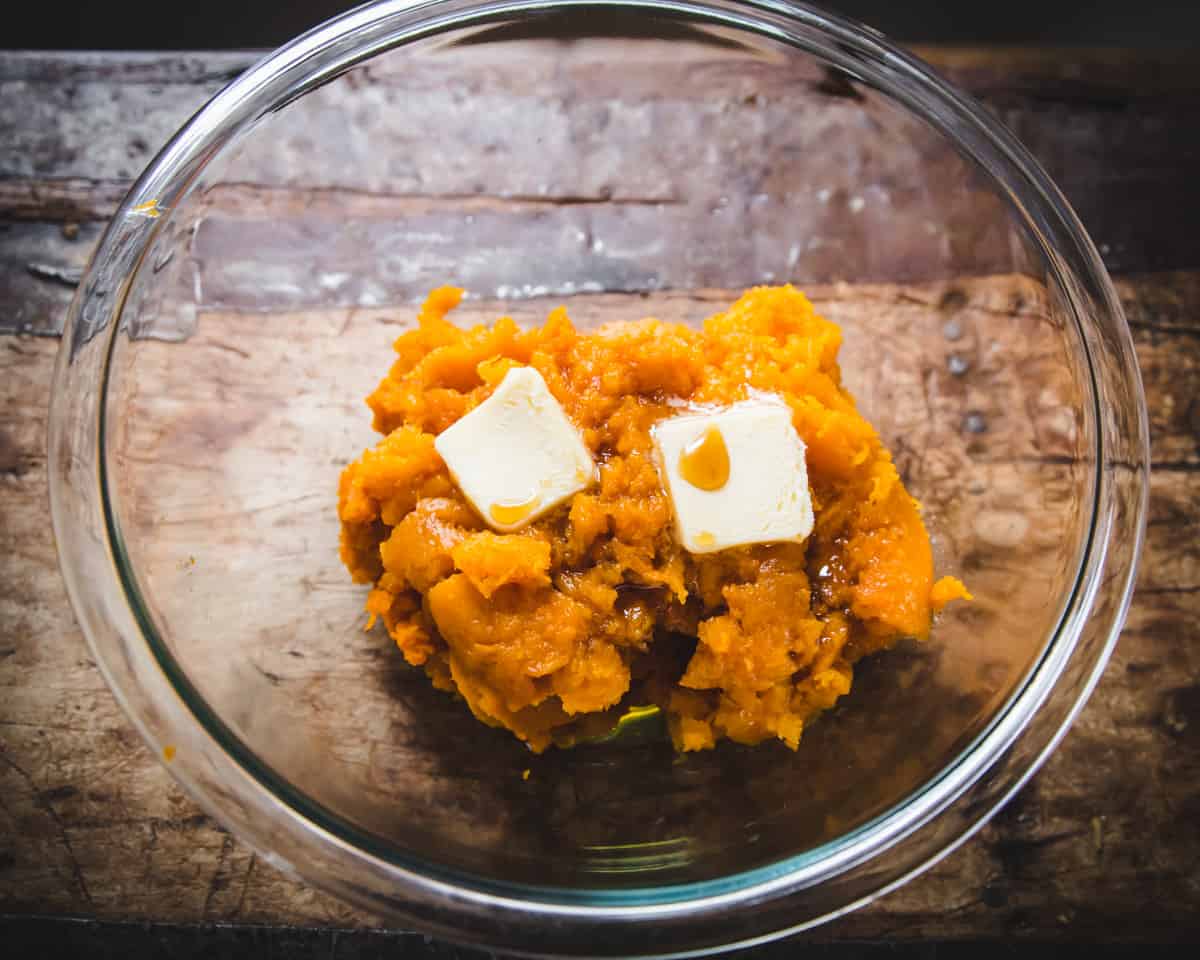 a glass bowl with butternut squash, butter, and maple syrup