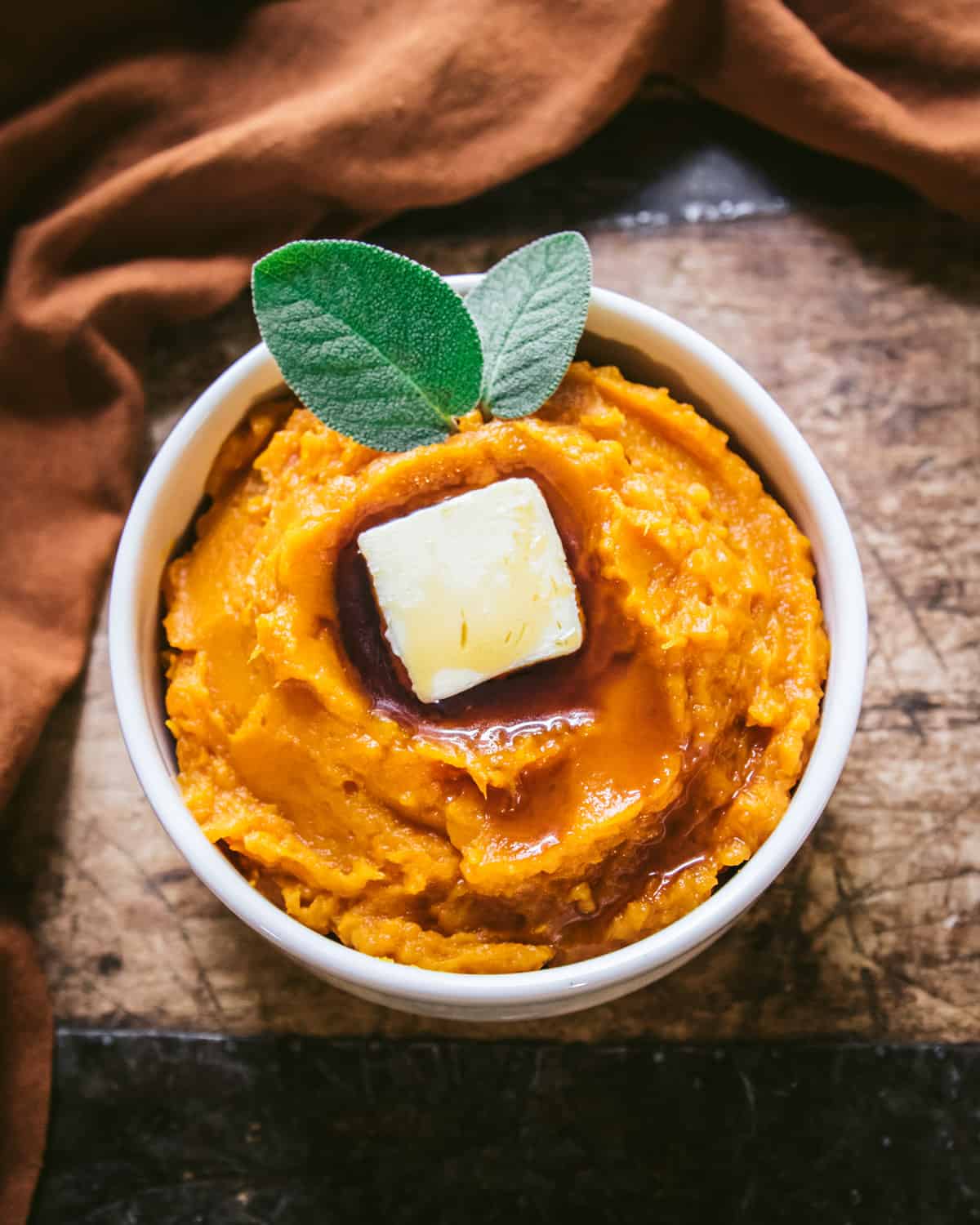 top view of a bowl of mashed butternut squash with a pat of butter and sage leaves