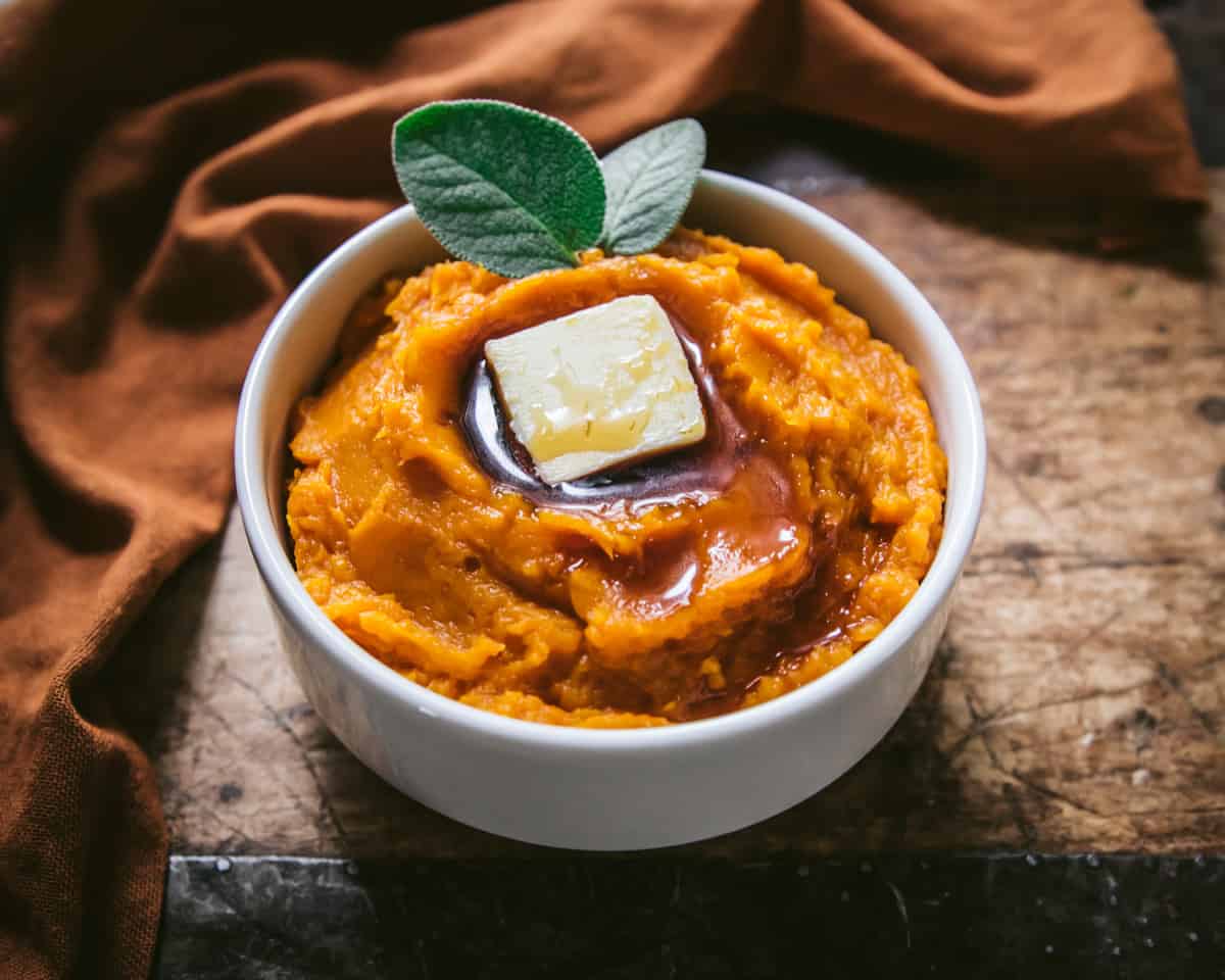 a bowl of mashed butternut squash with butter and maple syrup on a wooden table