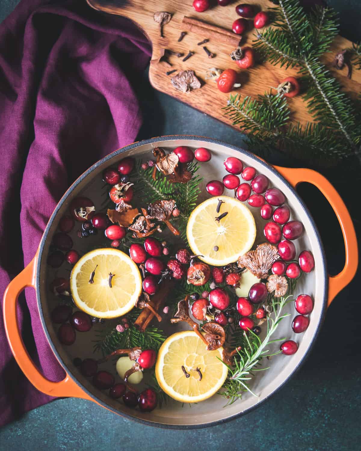a simemr pot filled with cranberries, orange slices, pine branches, candy cap mushrooms and spices