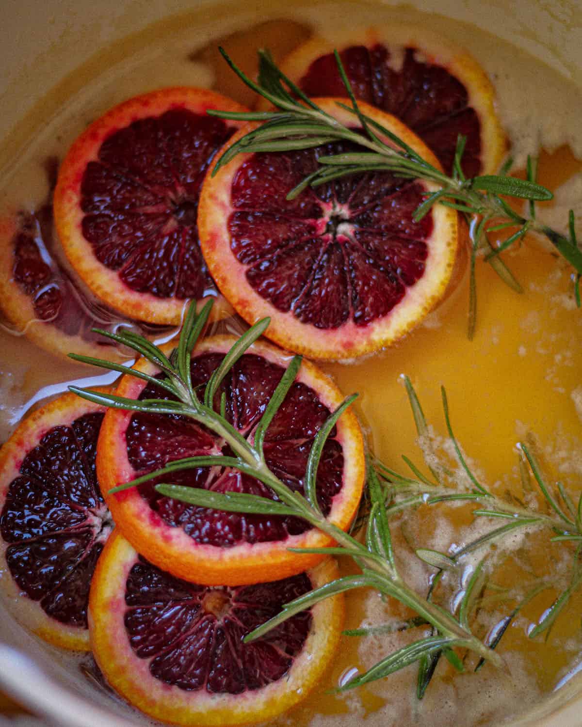 Slices of blood oranges and sprigs of rosemary simmering in a pan to make simple syrup.