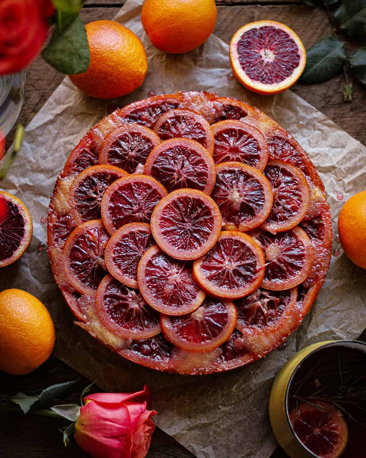Top view of finished blood orange upside down cake, with oranges and a rose surrounding it. 