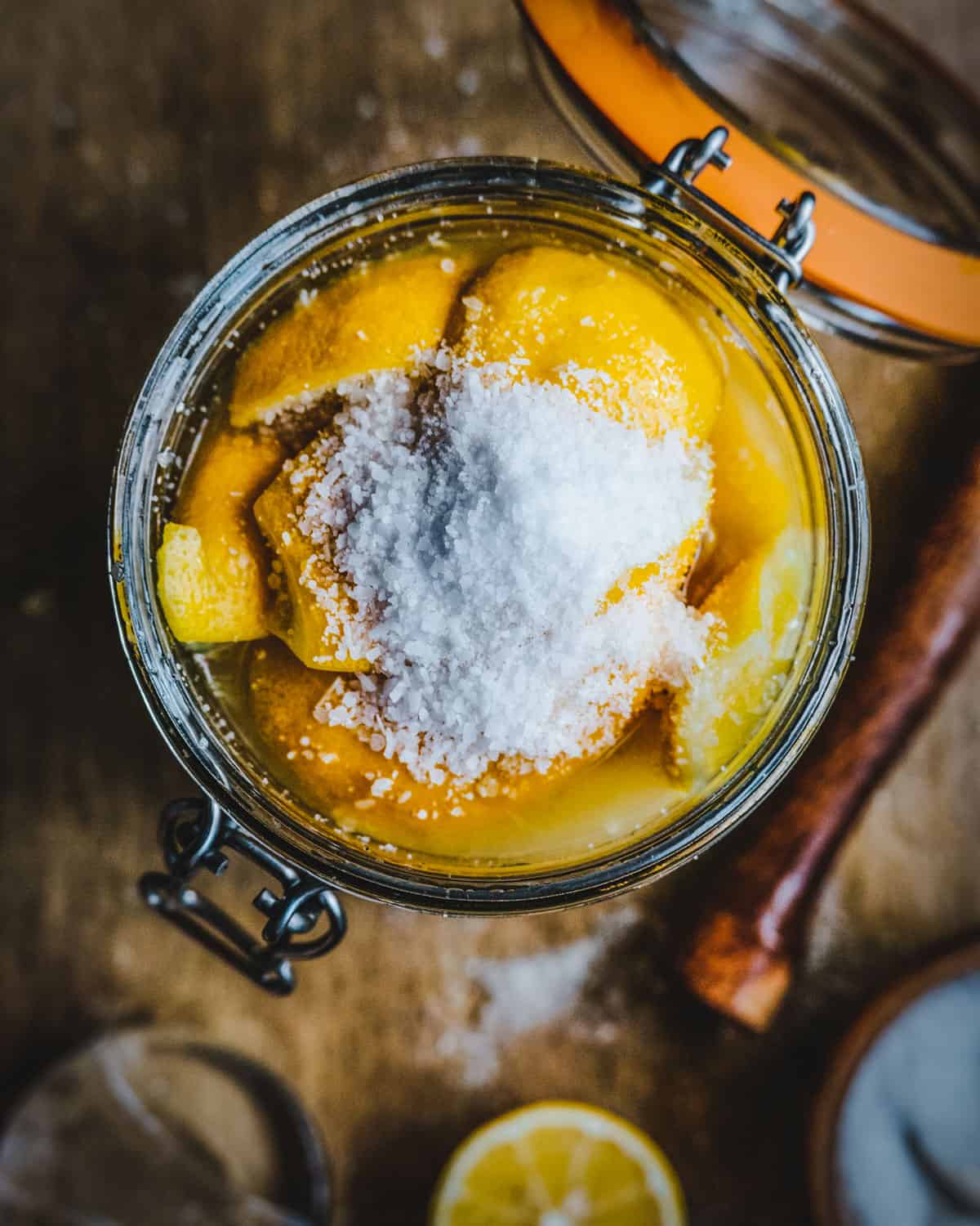 Top view of a jar with lemons, lemon juice, and topped with a small pile of salt. 