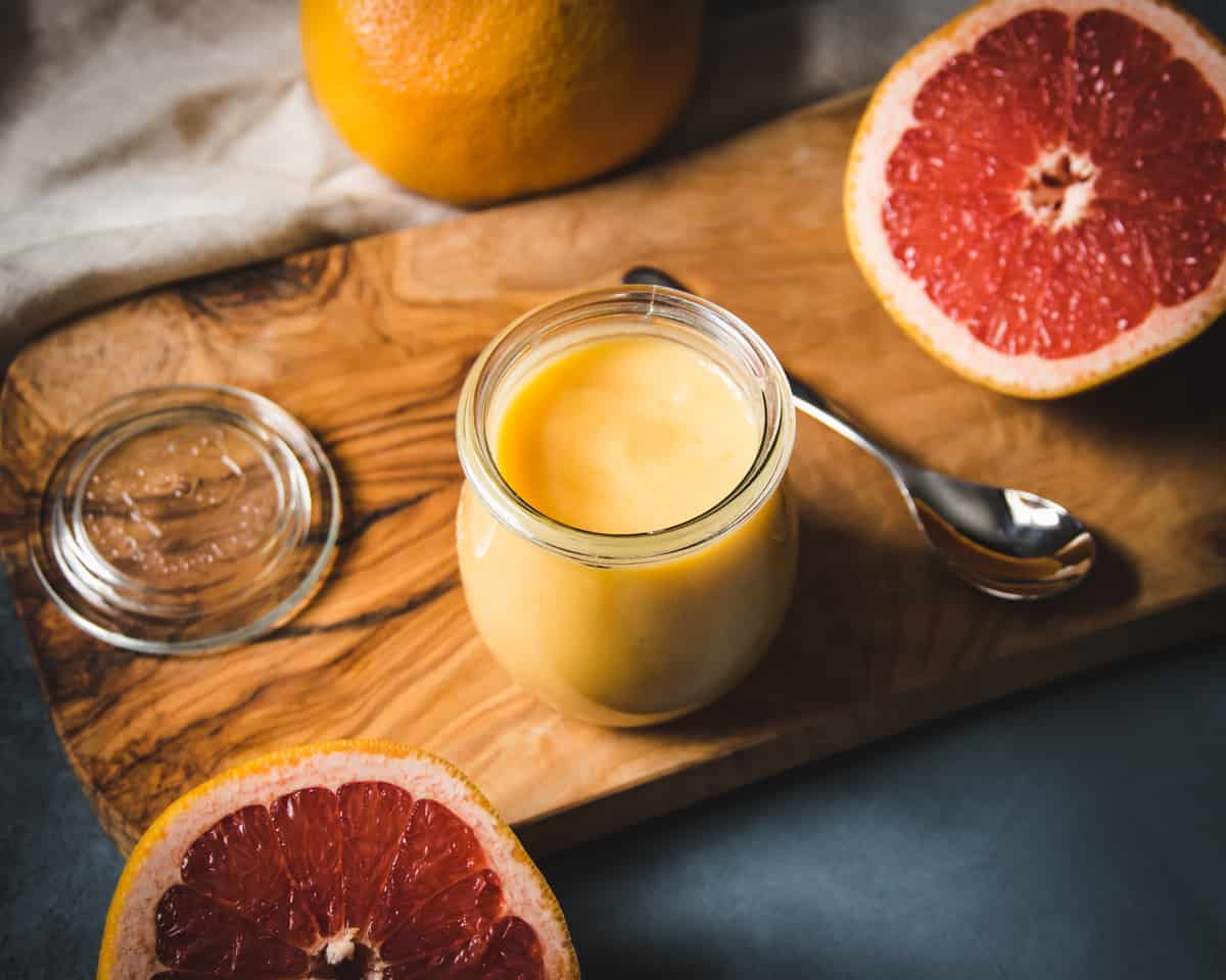 a jar of grapefruit curd on a wooden cutting board