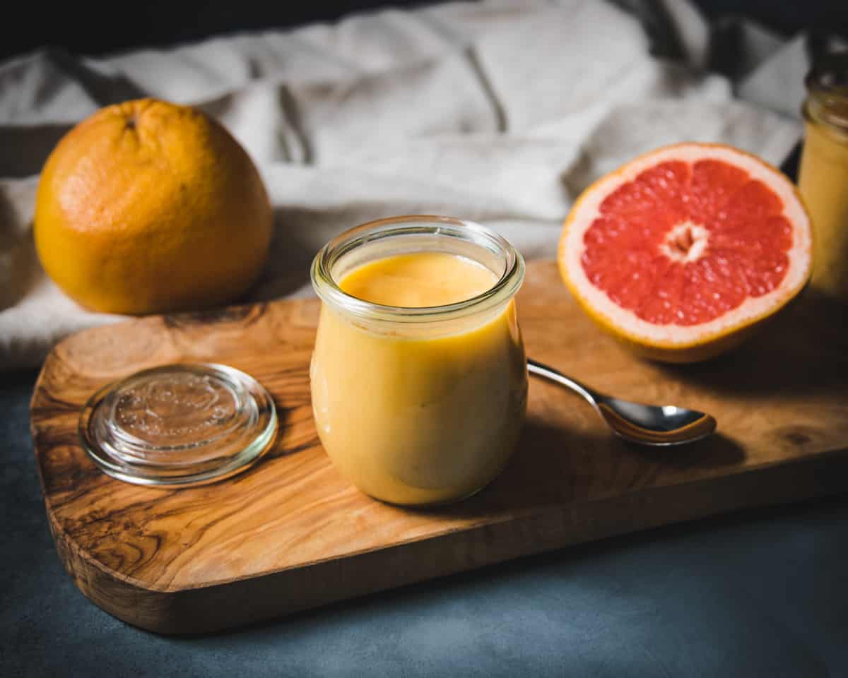 a jar of grapefruit curd on a wooden cutting board with cut red grapefruit