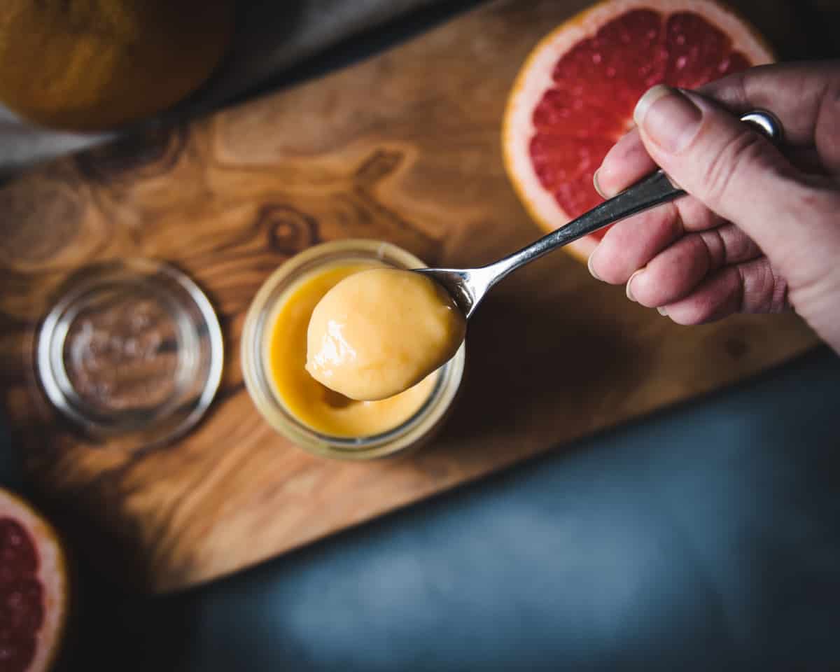 a hand holding a spoonful of grapefruit curd