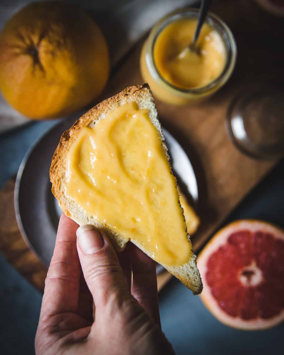 a hand holding a half piece of toast spread with grapefruit curd