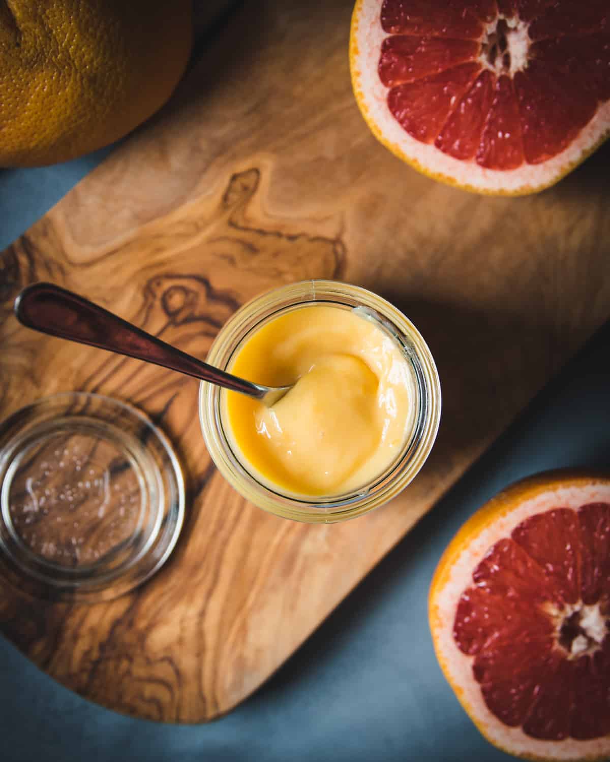 top view of a jar of grapefruit curd with a spoon and halved grapefruits on the table