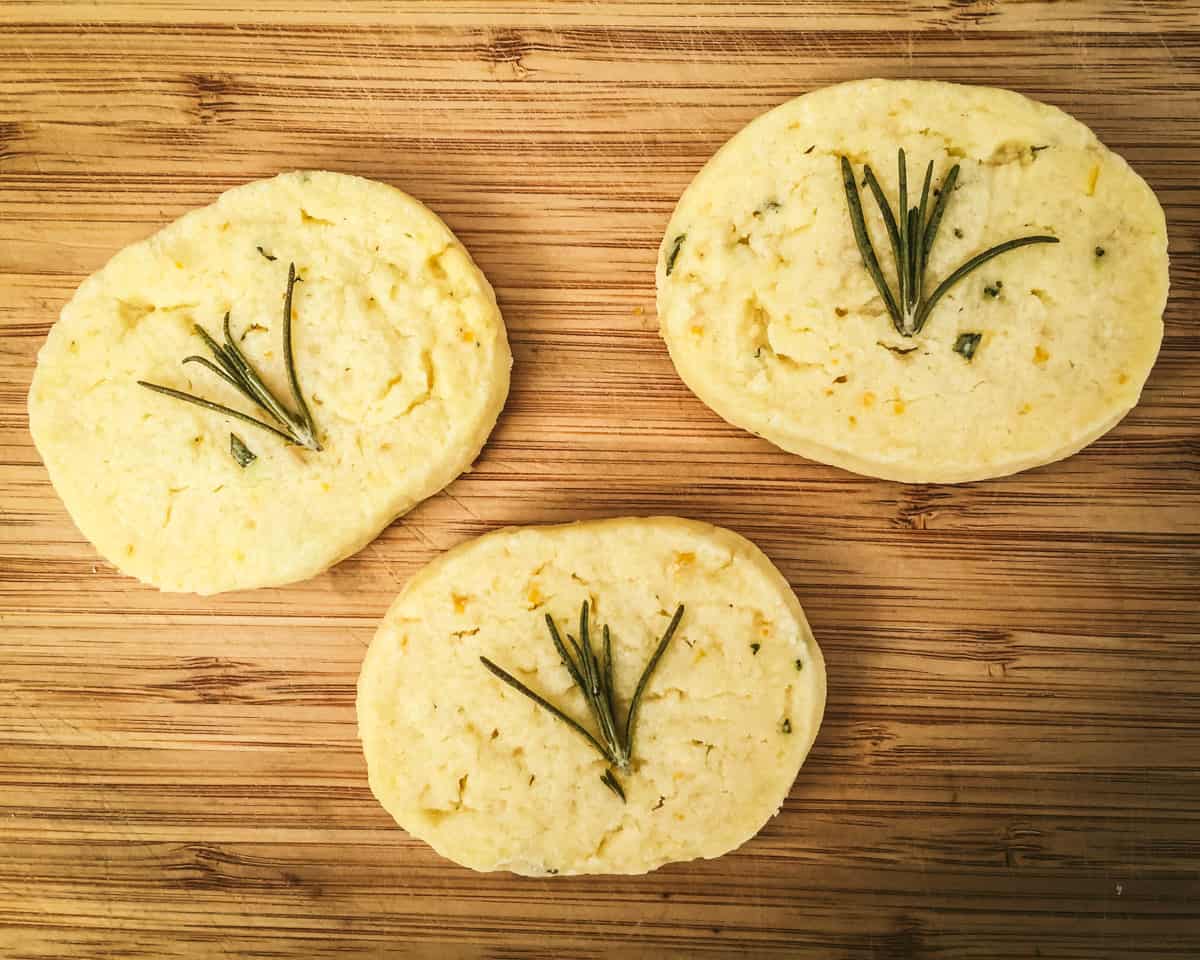 three lemon and rosemary shortbread cookies on a wooden cutting board