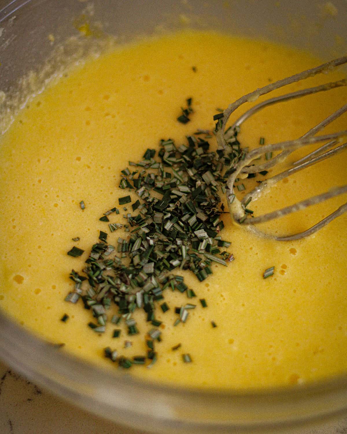 Wet ingredients in a bowl with a mixer adding in the chopped rosemary.