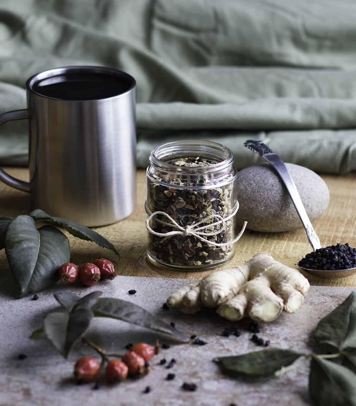 a jar of dried immune boosting tea blend with a mug, rose hips, and ginger