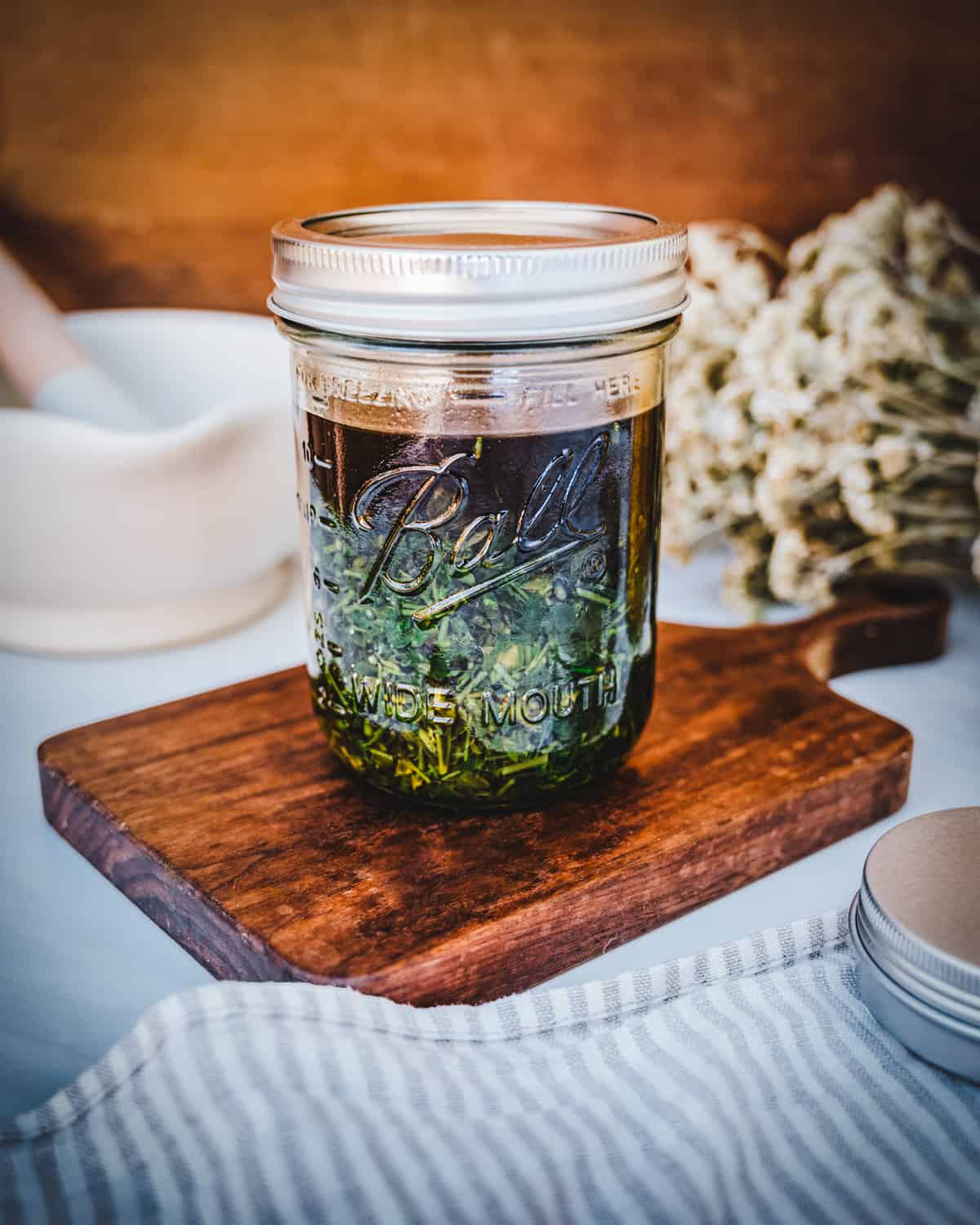 Chickweed infused oil in a glass jar sitting on a wood cutting board. 