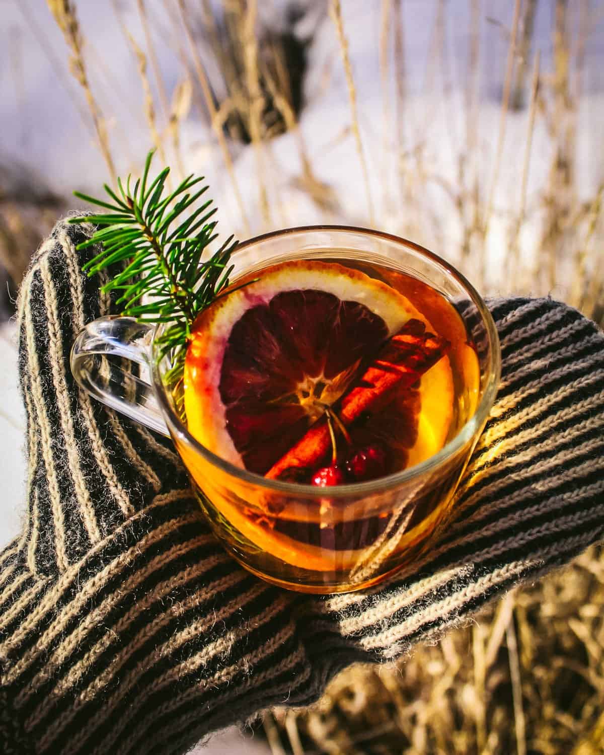 a hand with a mitten holding a conifer hot toddy