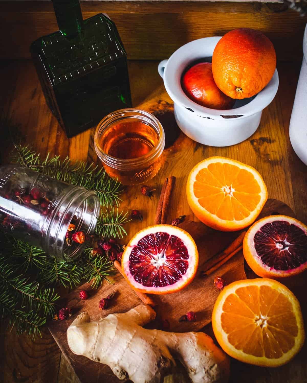 sliced oranges, conifer sprigs, rose hips, ginger, and honey on a table