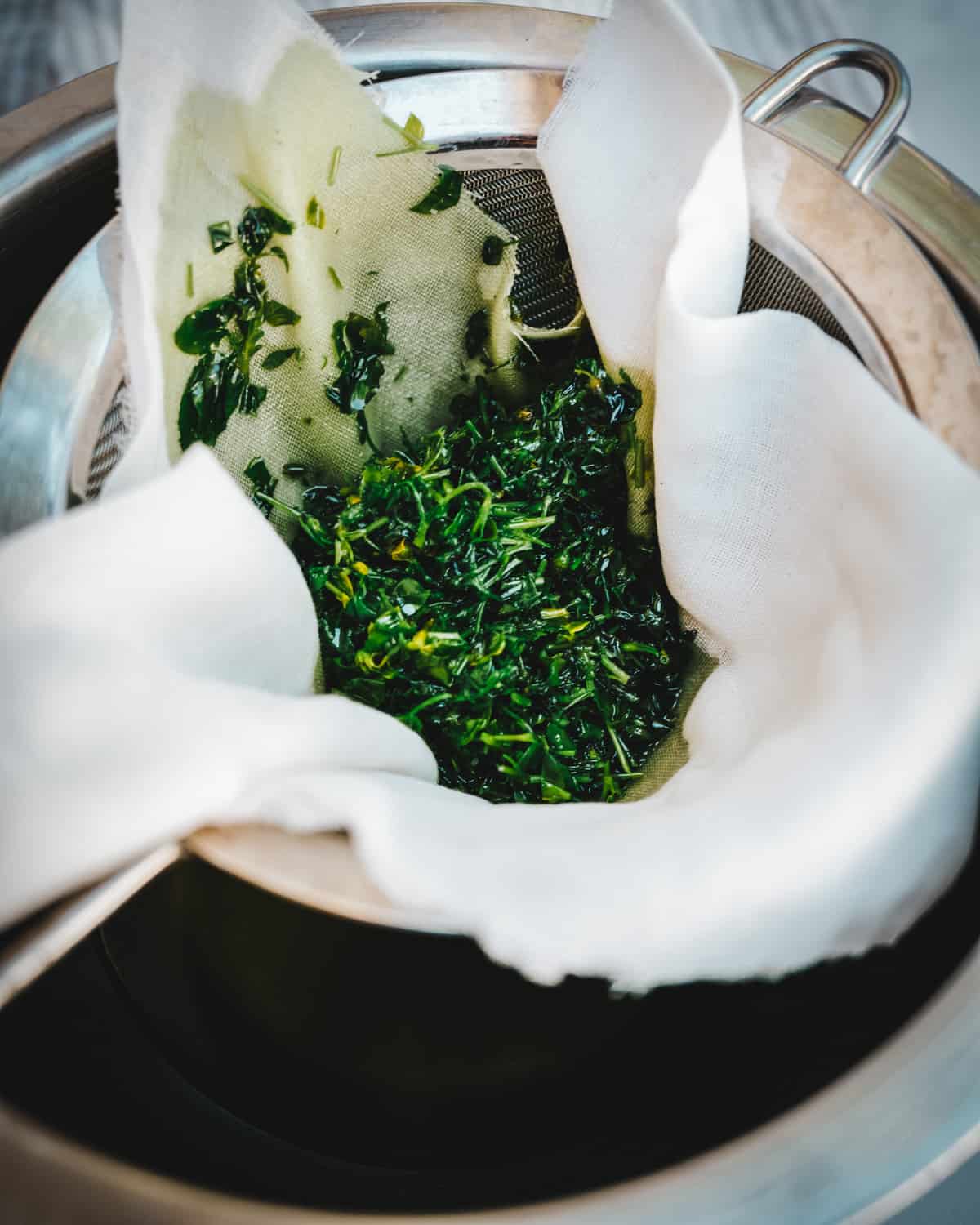 Chickweed being strained with a strainer and muslin cloth. 