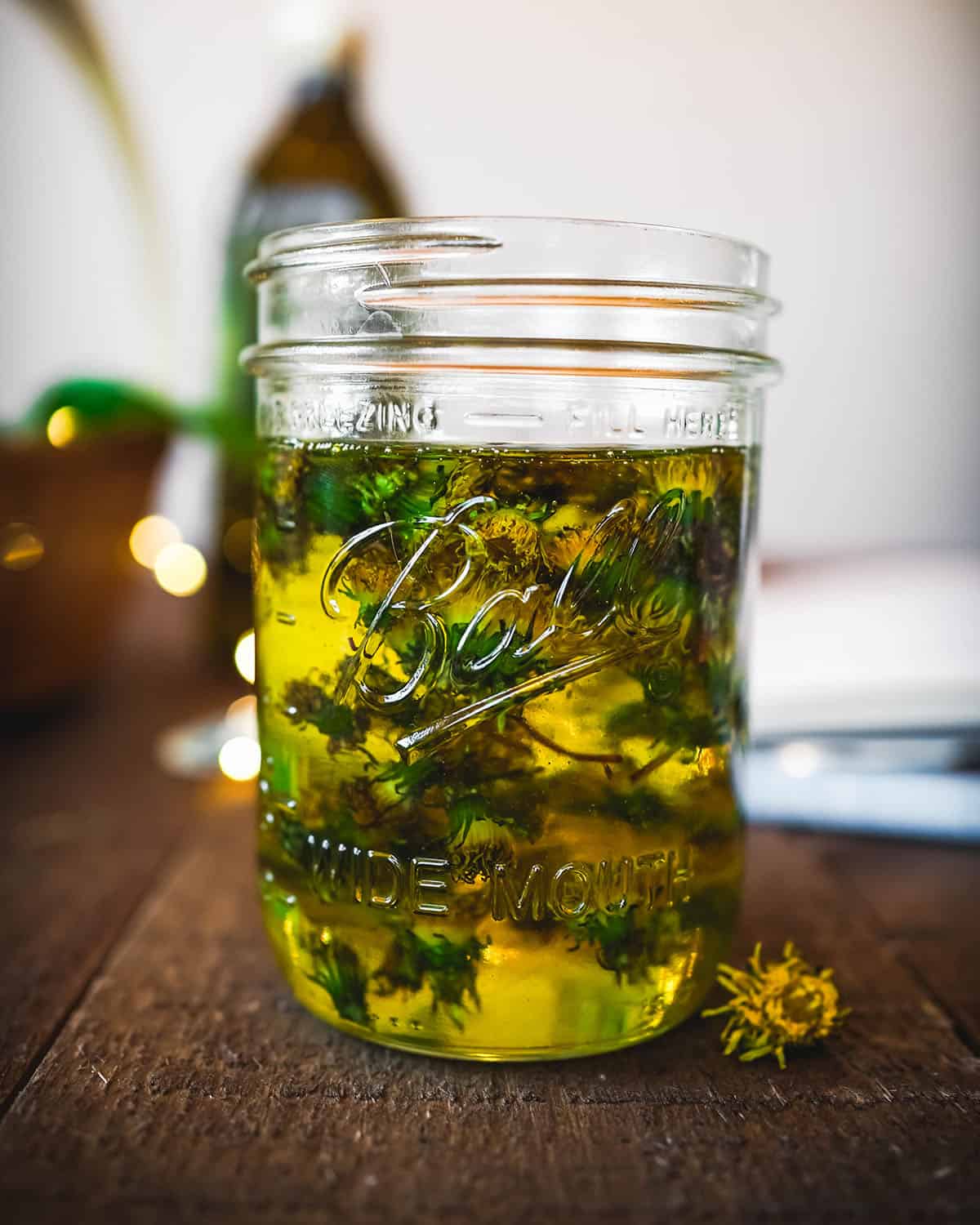 A glass jar filled with dried dandelions and oil to fill, sitting to infuse 