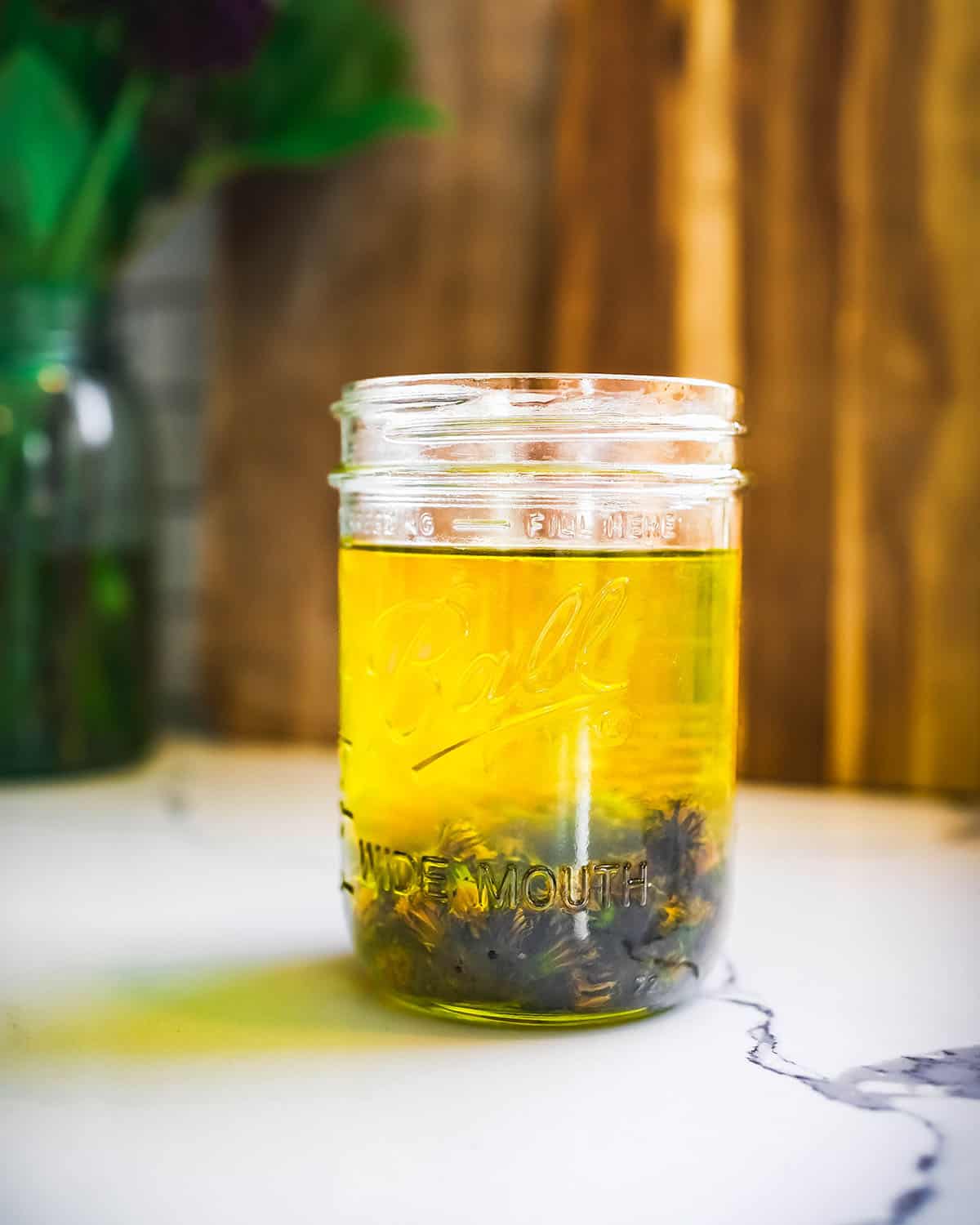 Finished infused dandelion oil, a vibrant golden oil with dandelions resting at the bottom of the jar. 